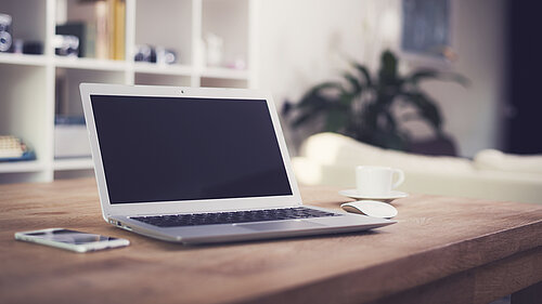 A laptop, phone and coffee cup on a table.